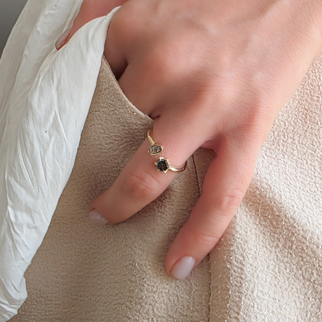 Lifestyle shot of a hand wearing the open yellow gold ring with contrasting salt and pepper diamonds.