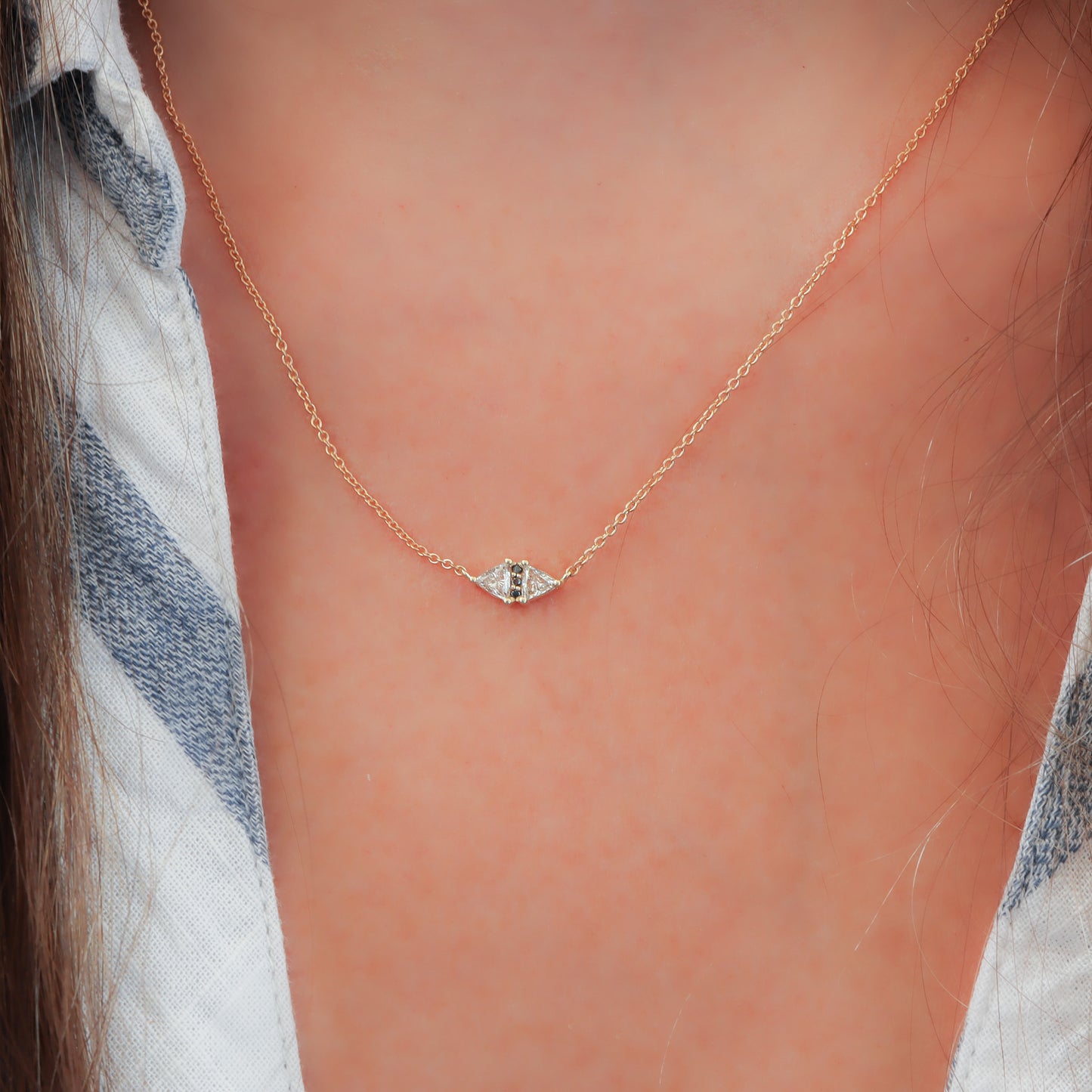 עיצוב גיאומטרי מהפנט של שרשרת זהב עם שני יהלומים בצורת משולש וביניהם שלושה יהלומים שחורים קטנים.