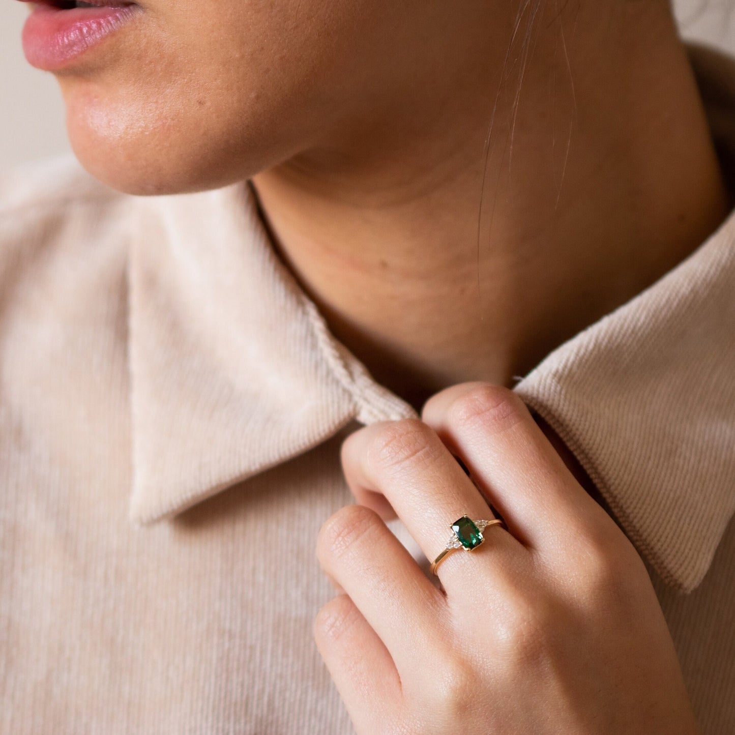 Woman's hand holding her shirt while wearing a Green Tourmaline Emerald Cut Ring with three small diamonds on each side