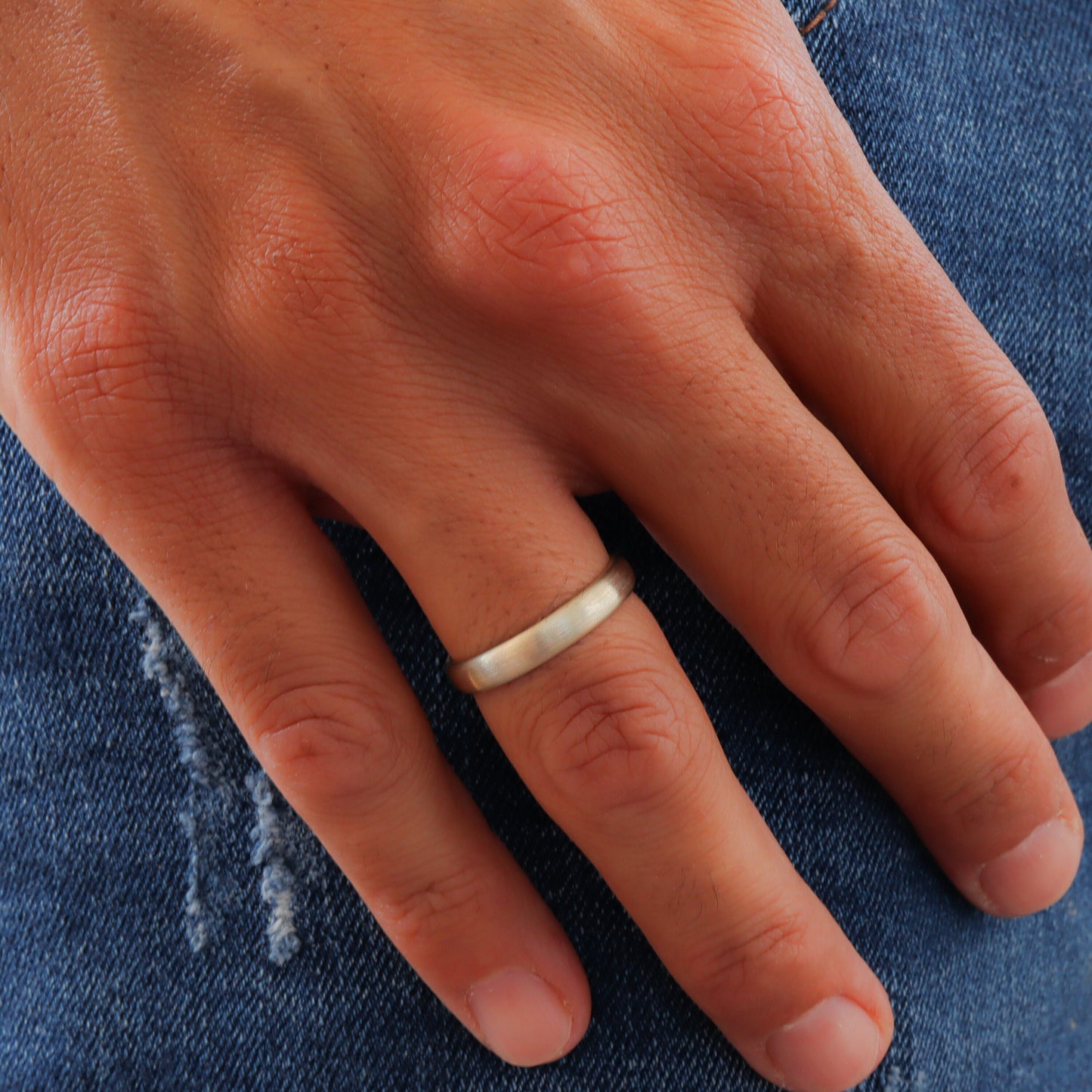 Close-up of a man's hand showcasing a rustic white gold wedding band.