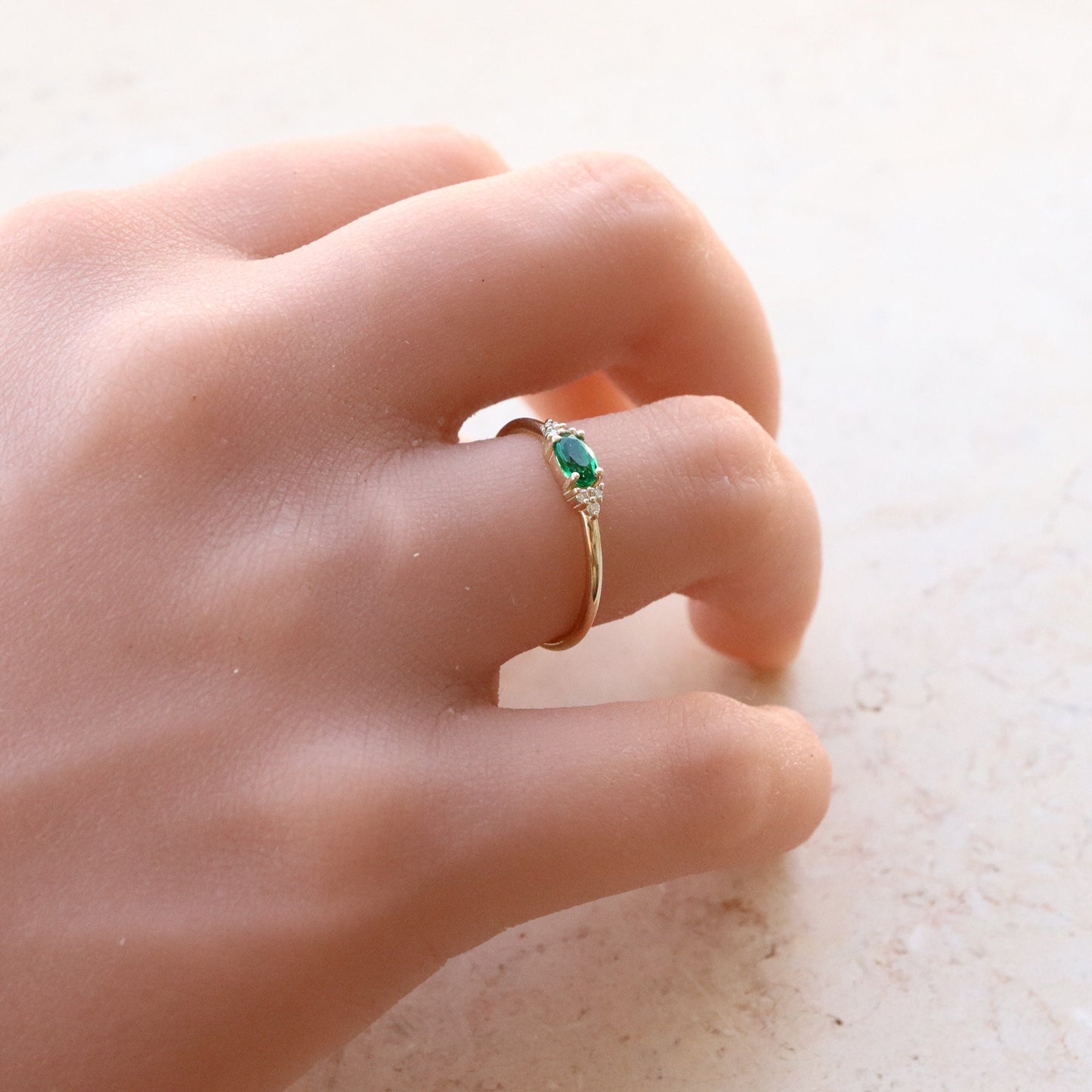 טבעת קטנה משובצת אבן ברקת ירוקה בחיתוך אליפסה מלווה בשישה יהלומים קטניםת משובצים בטבעת זהב צהוב.