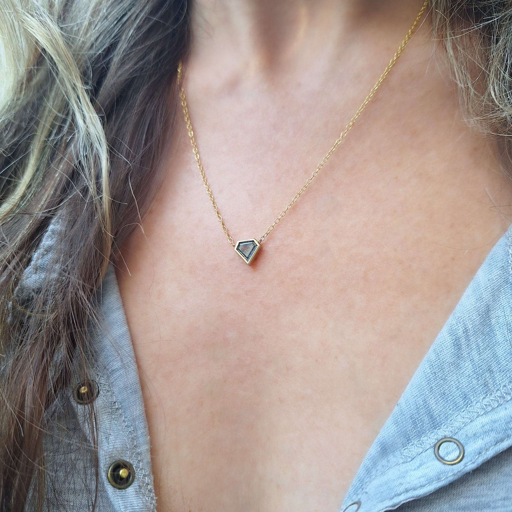 שרשרת יהלום מגן בגוון אפור עטוף במסגרת זהב.