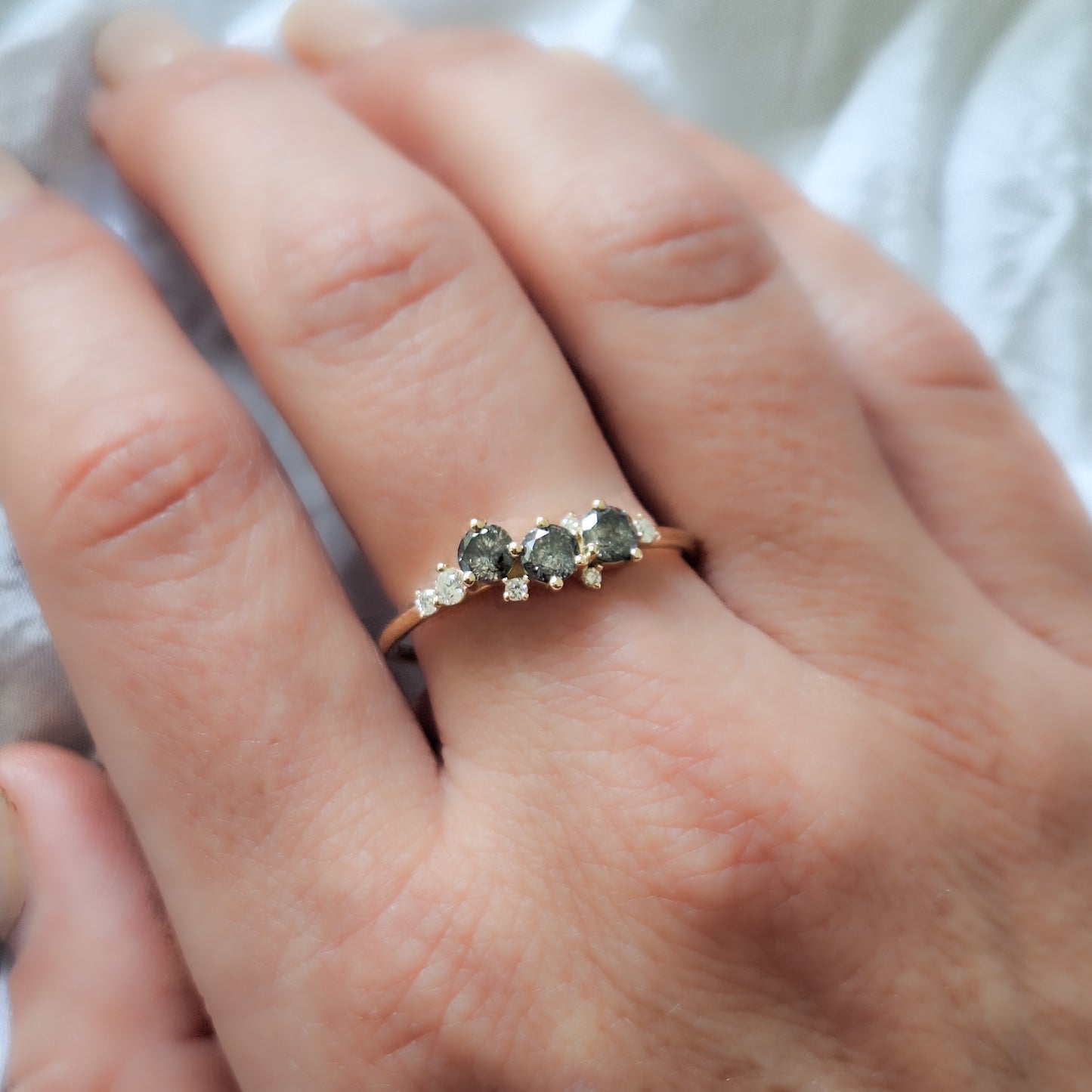 טבעת קלאסטר מעוצבת על אצבע, המציגה את השילוב בין גווני האפור של יהלומי המלח-פלפל לניצנוץ של היהלומים הלבנים על רקע זהב צהוב.