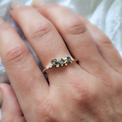 טבעת קלאסטר מעוצבת על אצבע, המציגה את השילוב בין גווני האפור של יהלומי המלח-פלפל לניצנוץ של היהלומים הלבנים על רקע זהב צהוב.