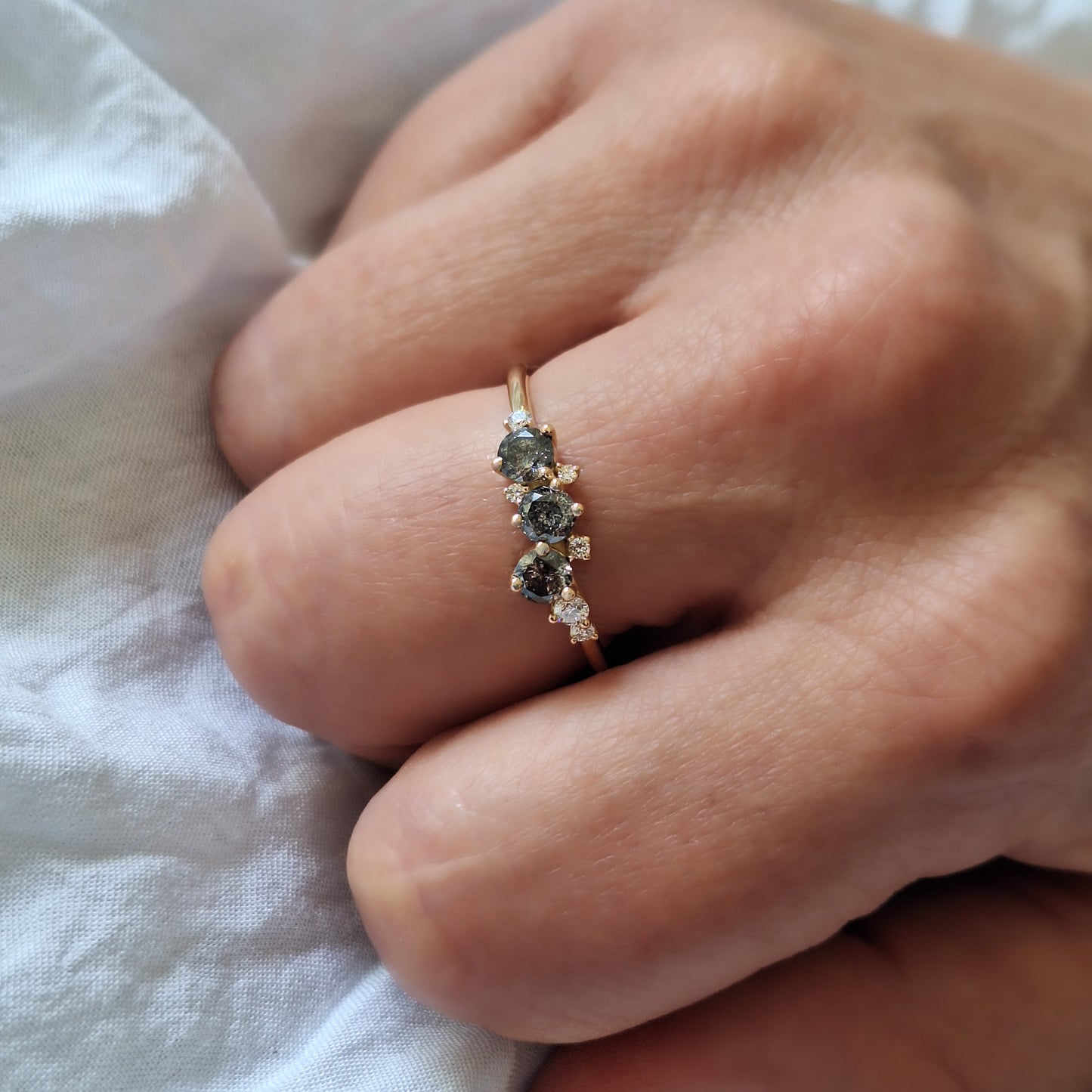 מבט מזווית על טבעת קלאסטר משובצת יהלומי מלח-פלפל ויהלומים לבנים על אצבע, המדגיש את המבנה הגיאומטרי המדויק ואת השתקפות האור מהזהב הצהוב.