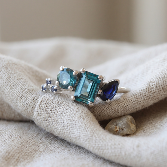 White gold gemstone ring featuring topaz and sapphire in an asymmetrical layout.