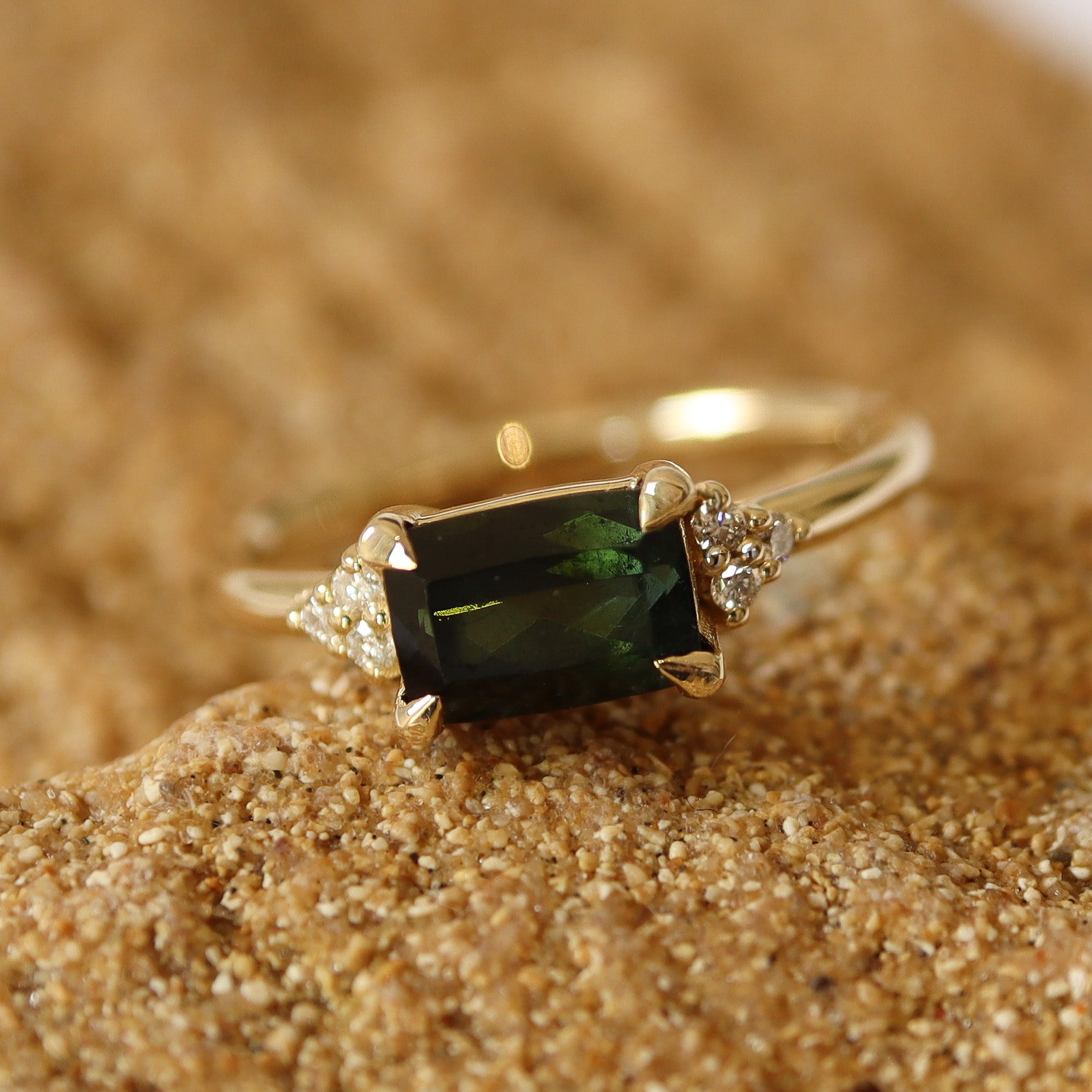 Dark green tourmaline ring set in yellow gold with six small diamonds on each side, displayed on a natural stone background.