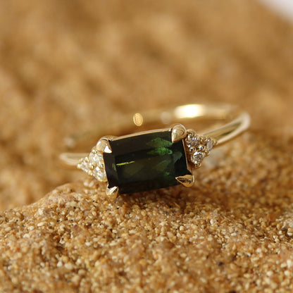 Dark green tourmaline ring set in yellow gold with six small diamonds on each side, displayed on a natural stone background.