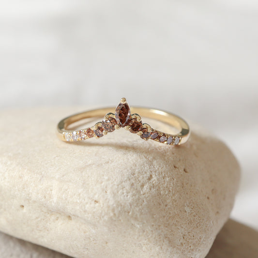 טבעת זהב בצורת V (שברון) משובצת יהלומים במעבר גוונים מחום במרכז ללבן בצדדים, מונחת על אבן טבעית.