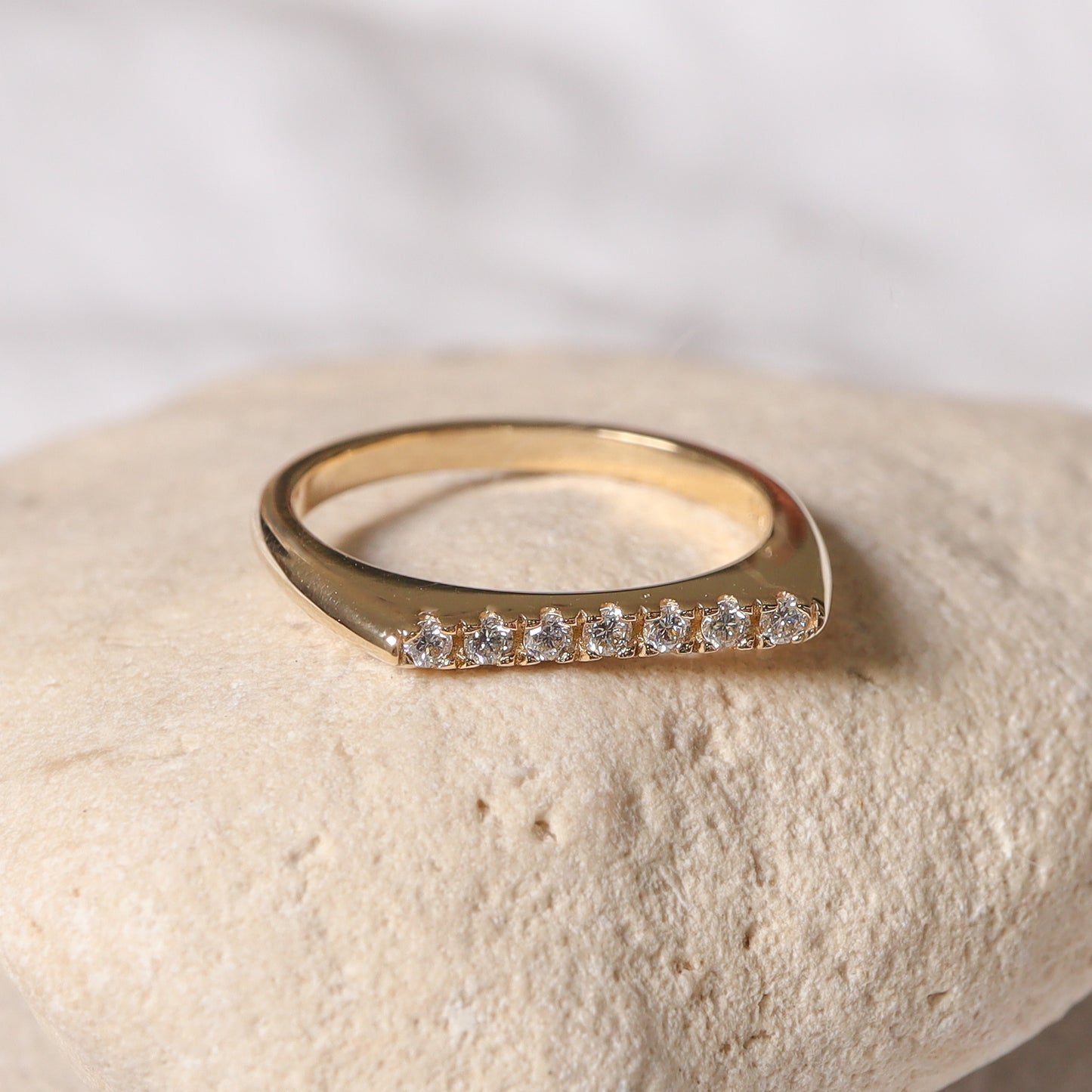 טבעת זהב שטוחה עם שורת יהלומים מונחת על אבן, המדגישה את הקווים הישרים והנקיים של העיצוב.