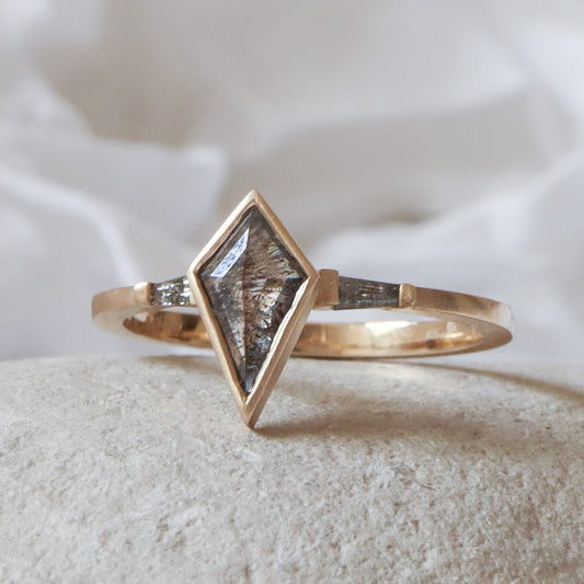 טבעת זהב צהוב בגימור מט עם יהלום מרכזי בצורת דלתון ושני יהלומים בצורת טרפז בצדדים, כולם בגווני אפור מלח-פלפל.