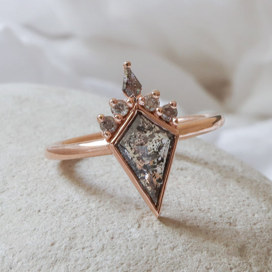 טבעת זהב אדום 14 קראט במבנה כתר, במרכזה יהלום מלח-פלפל אפור בחיתוך עפיפון ומתחתיו חמישה יהלומים קטנים בגווני אפור על רקע לבן.