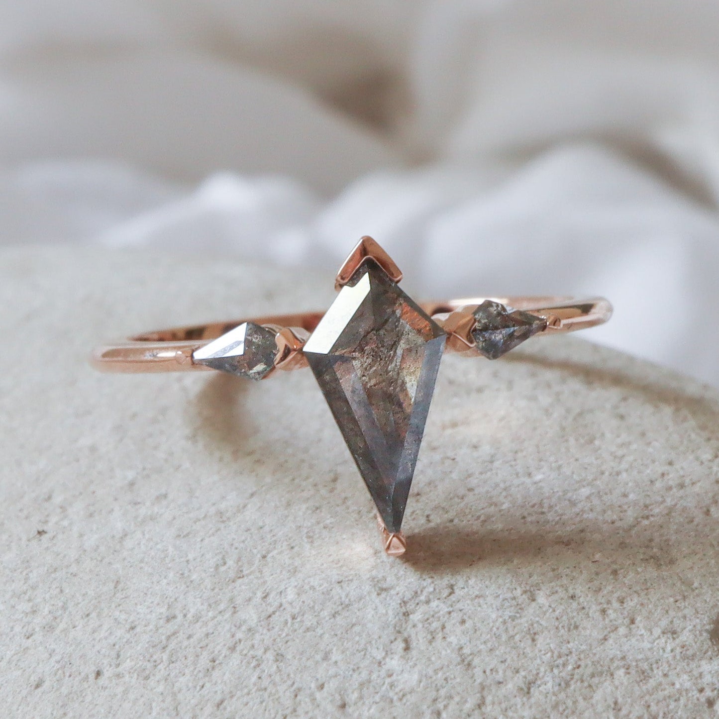 טבעת זהב עם שלושה יהלומי מלח-פלפל בחיתוך דלתון בשיבוץ חצי כוס המגן על הקצוות ומשאיר את צדי היהלום חשופים.