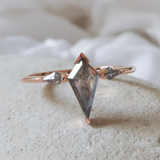 טבעת זהב עם שלושה יהלומי מלח-פלפל בחיתוך דלתון בשיבוץ חצי כוס המגן על הקצוות ומשאיר את צדי היהלום חשופים.