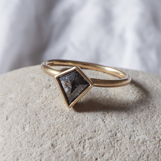 טבעת יהלום משובצת יהלום בצורת דלתון בגוון אפור כהה, הטבעת זהב צהוב עם גימור מט גולמי.