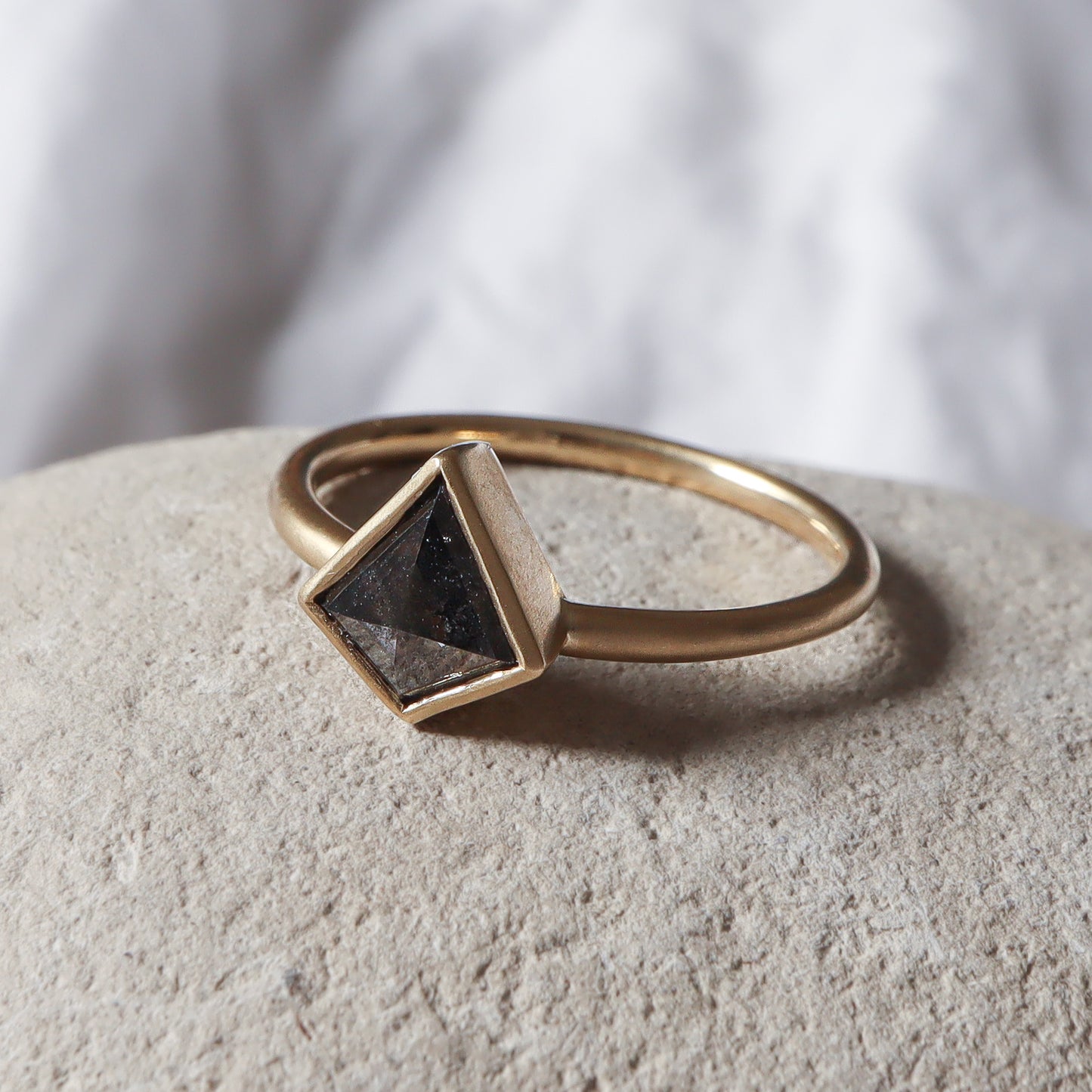 טבעת דלתון בגימור מט מונחת על אבן, המבליטה את המראה הגולמי והנקי של העיצוב.