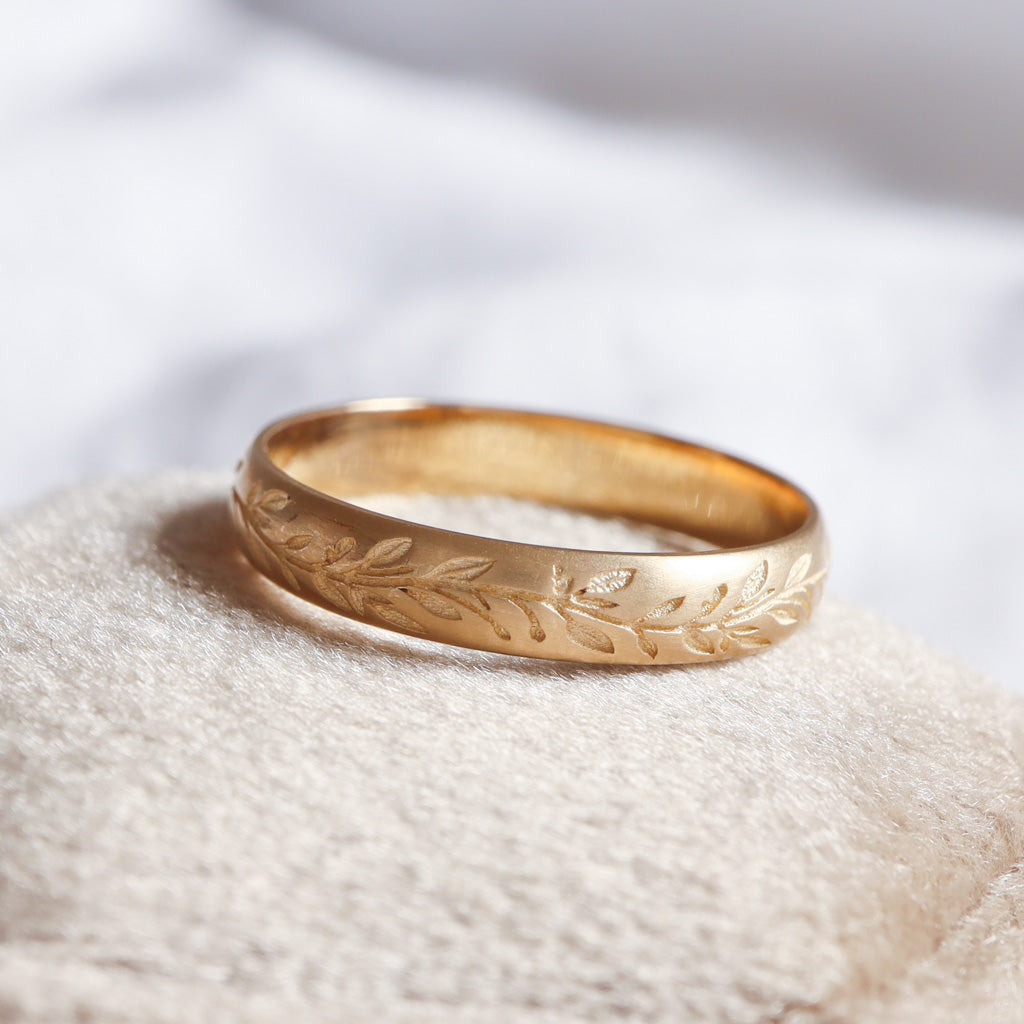 טבעת נישואין מזהב 14 קראט בעיצוב עלי דפנה בגימור מחוספס מונחת על אבן טבעית