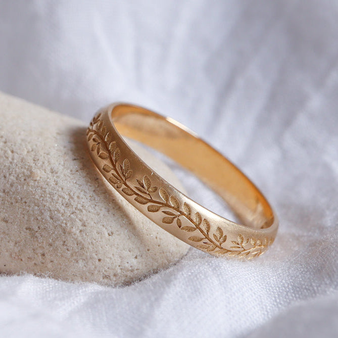 טבעת נישואים, מעוטרת בהשראת הטבע, עשויה מזהב צהוב ומונחת על רקע לבן.