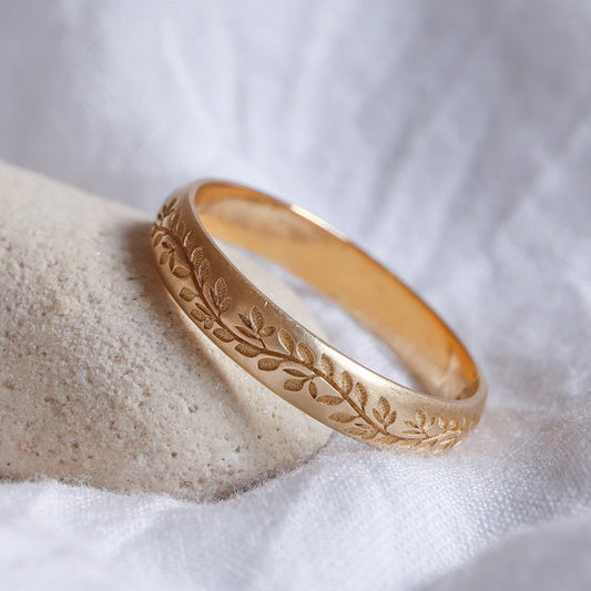 טבעת נישואים, מעוטרת בהשראת הטבע, עשויה מזהב צהוב ומונחת על רקע לבן.