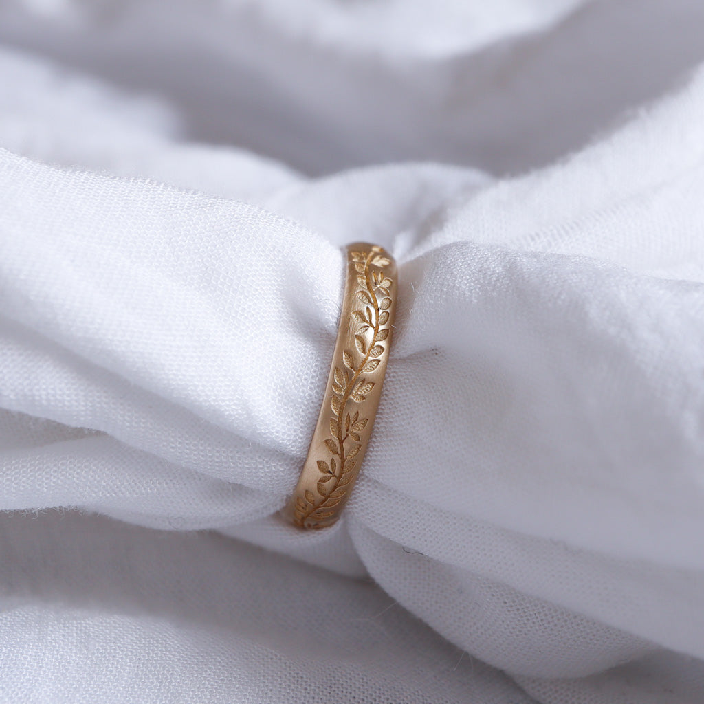 טבעת נישואים מיוחדת ועדינה עם ריטות של עלים, מונחת על רקע לבן.