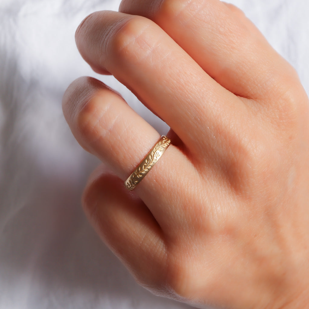 חריטות עלי עץ המורינגה על טבעת נישואים מונחת על יד.