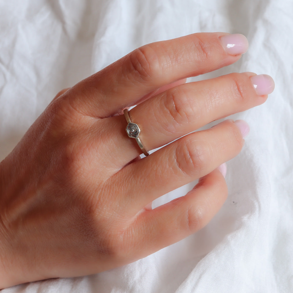 Delicate champagne gold hexagon salt and pepper diamond ring on a finger.