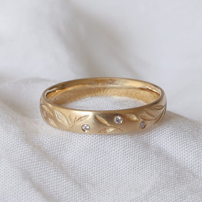 Nature inspired wedding band with scattered leaves and diamonds on a gold band.