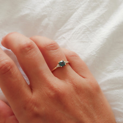 A close-up lifestyle shot of the gold turquoise sapphire ring on the finger, highlighting the contrast with the skin.