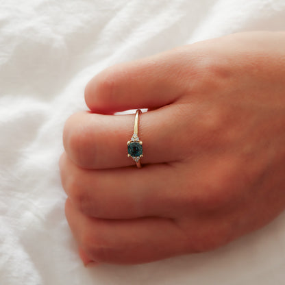 A view of the cushion cut teal sapphire ring on a finger, showcasing its delicate and elegant appearance on the hand.
