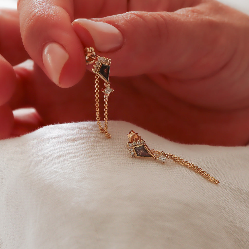 A detailed shot of the kite salt and pepper diamond earring held in hand, showing the delicate chain and princess cut diamond drop.