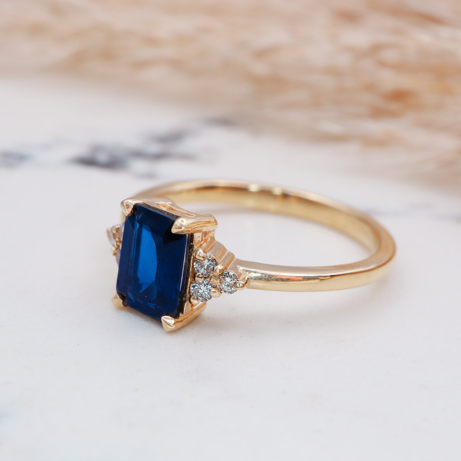 Side view of the Stunning Blue Sapphire Engagement Ring on white marble, highlighting its intricate details.