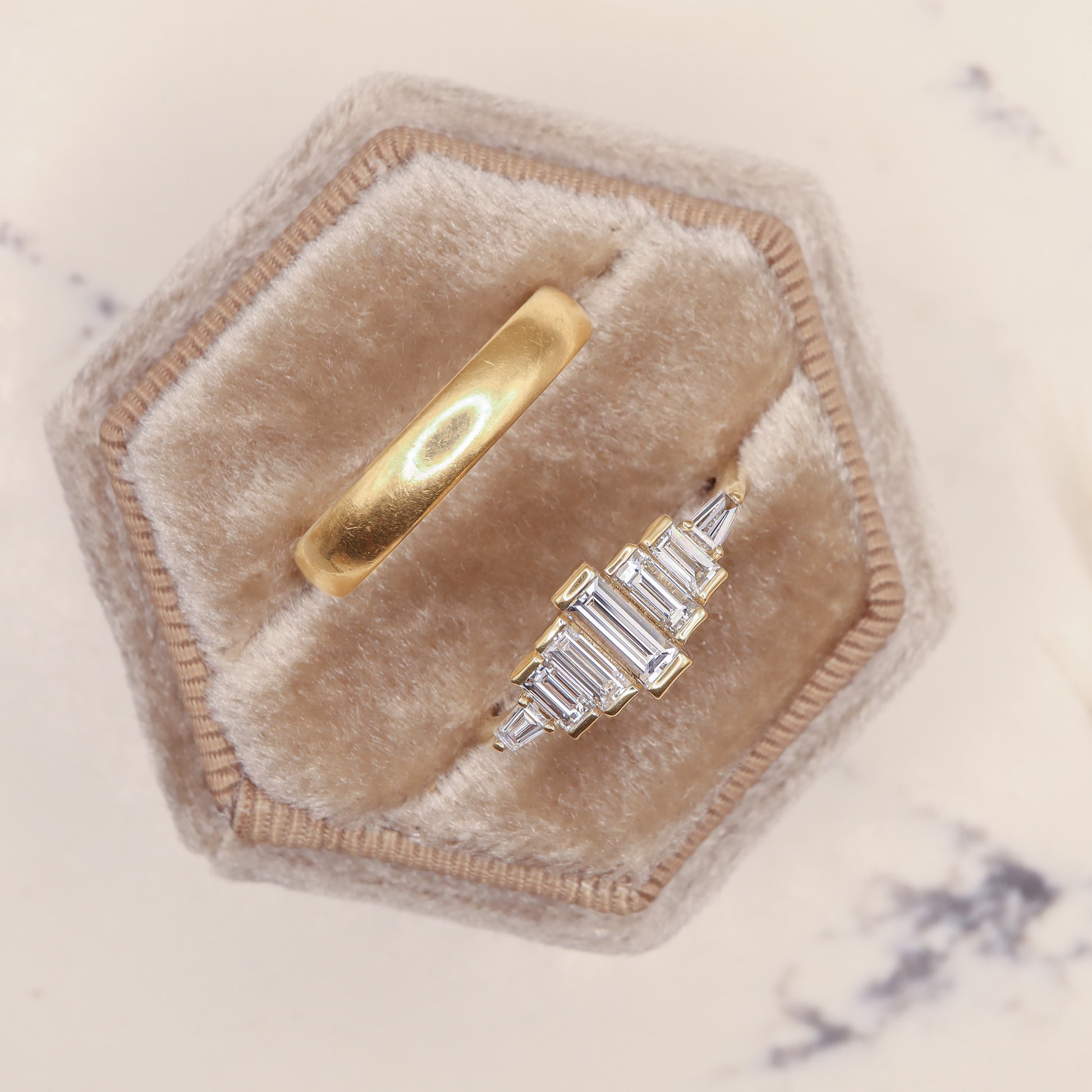 Diamond Baguette Gold Ring with Bezel-Set Vertical Step Design in a jewelry box beside a gold wedding band.