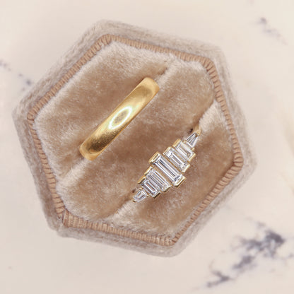 Diamond Baguette Gold Ring with Bezel-Set Vertical Step Design in a jewelry box beside a gold wedding band.