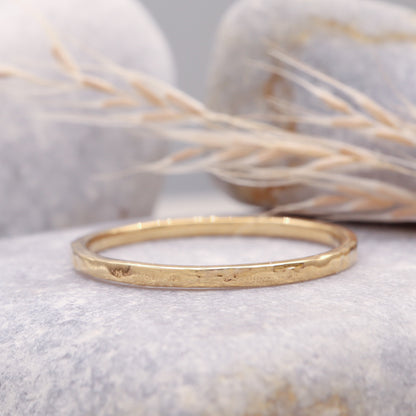 Hammered gold wedding ring displayed on a grey stone surface.