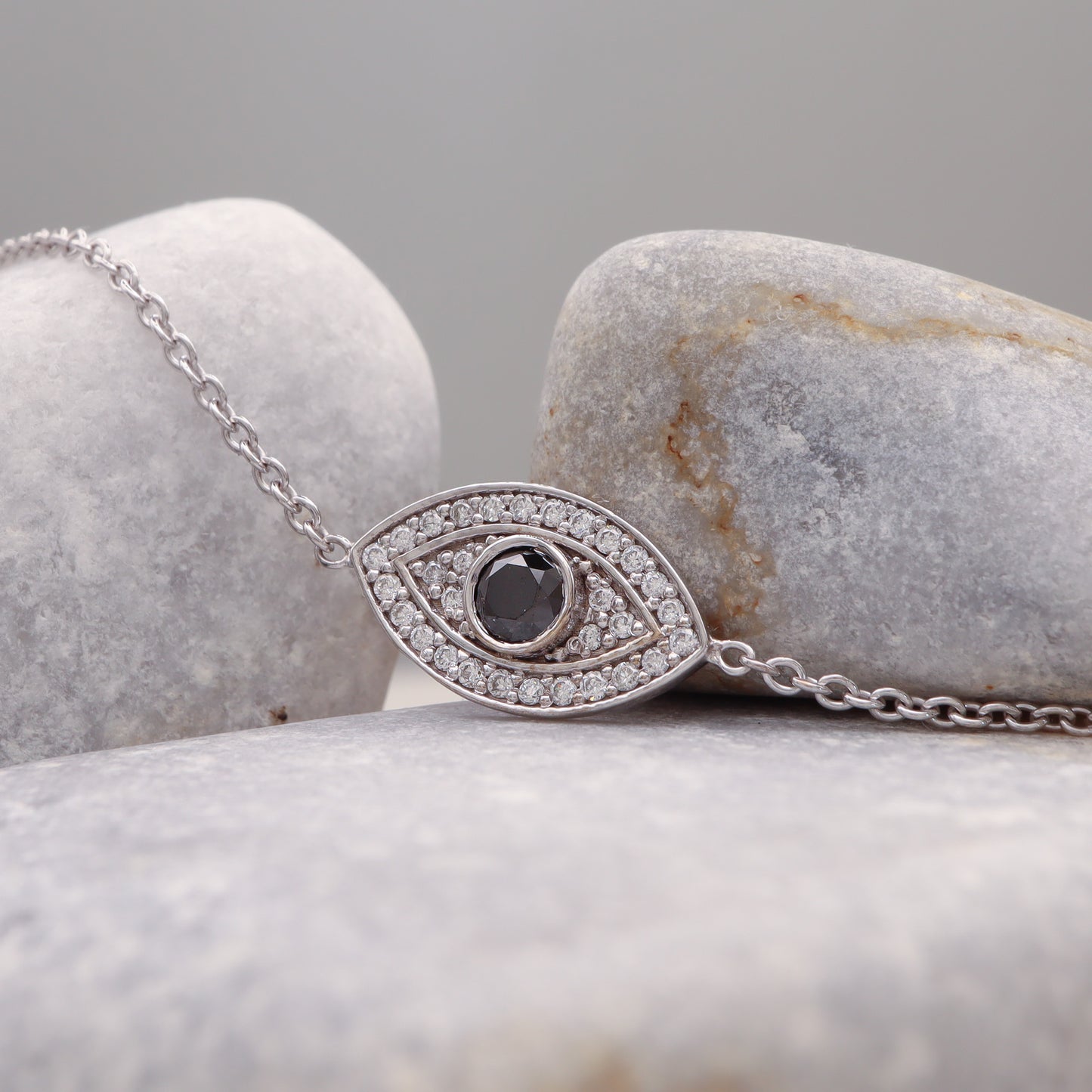 White gold Evil Eye Bracelet adorned with Black & White Diamonds, elegantly displayed on a grey stone.