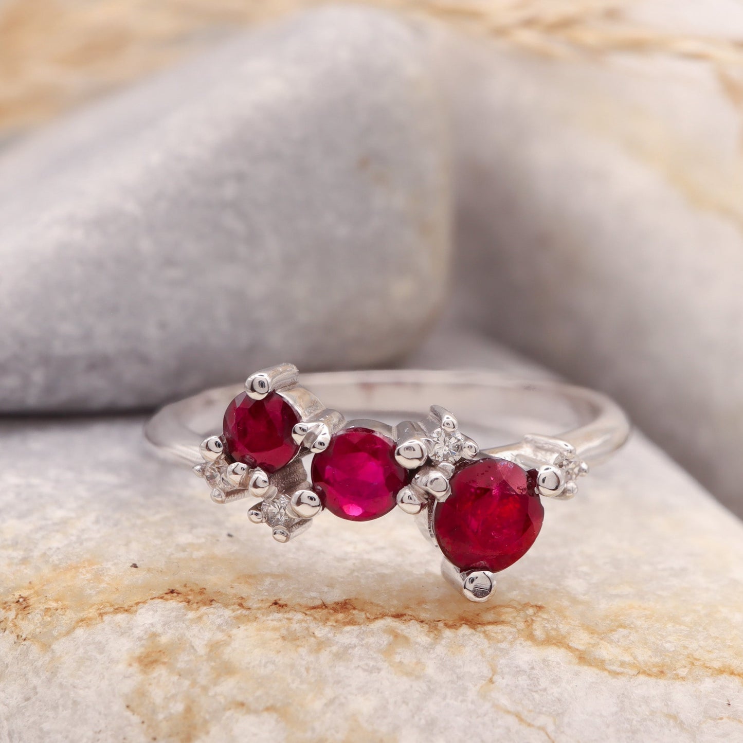 3 Ruby and 4 small Diamond cluster ring in solid white gold, showcased on a grey stone.