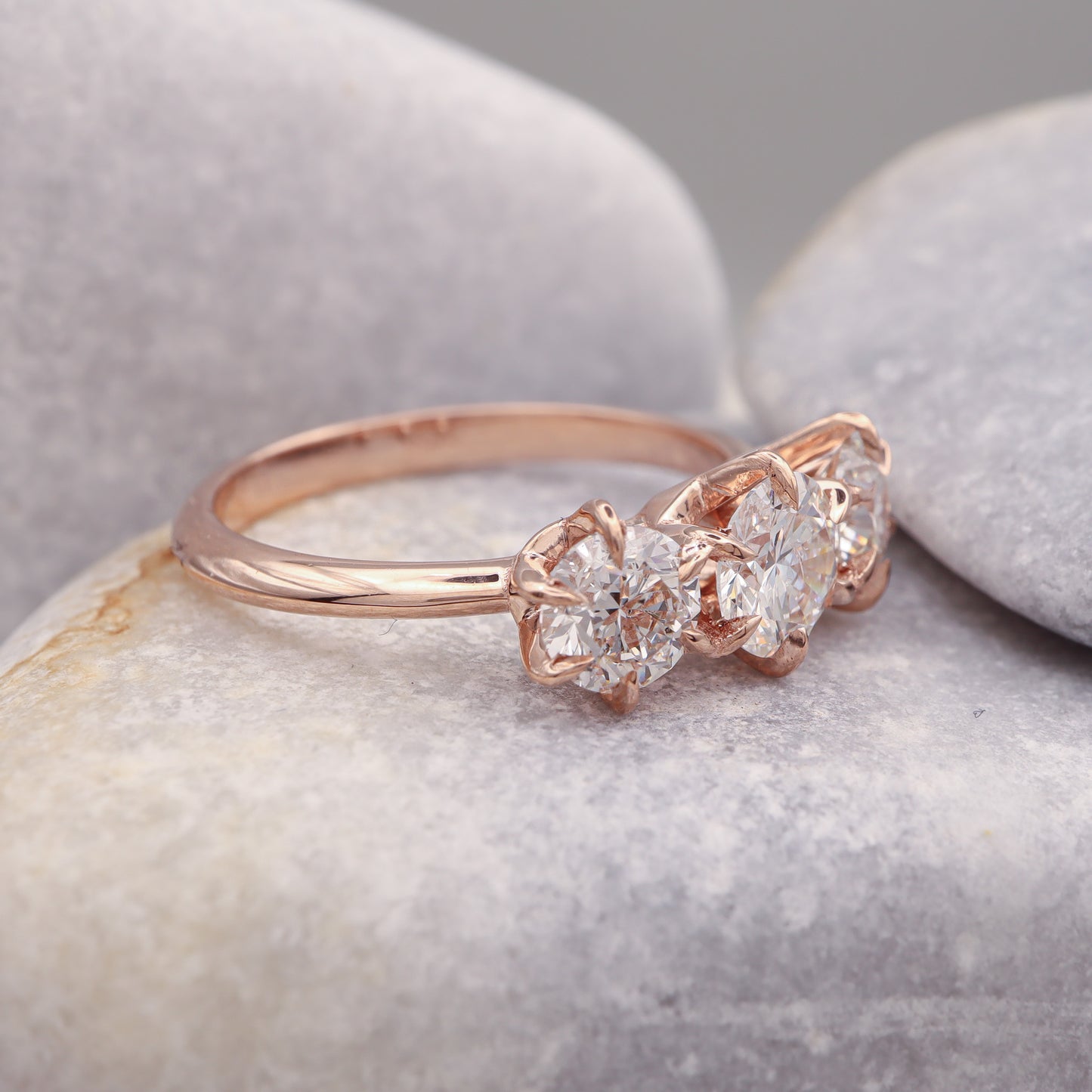 Profile view of a three-diamond rose gold ring with an elegant 6-prong design, showcased on a grey stone.