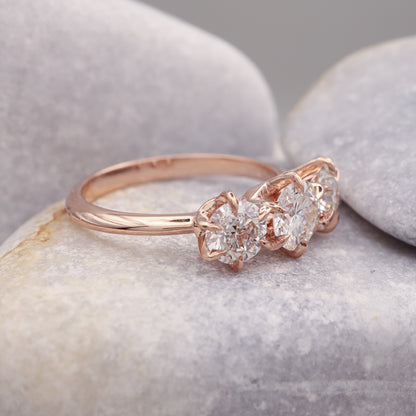 Profile view of a three-diamond rose gold ring with an elegant 6-prong design, showcased on a grey stone.