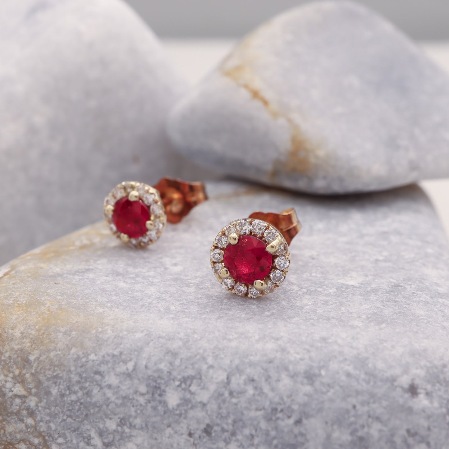 Ruby Halo Studs, surrounded by genuine diamonds, in gold, elegantly displayed on a grey stone.