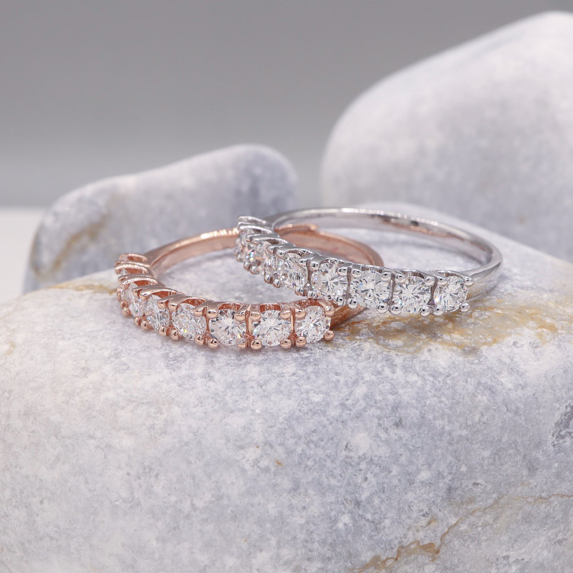 Artistic display of the rose and white gold rings, united in their brilliance, set against a sleek grey stone.