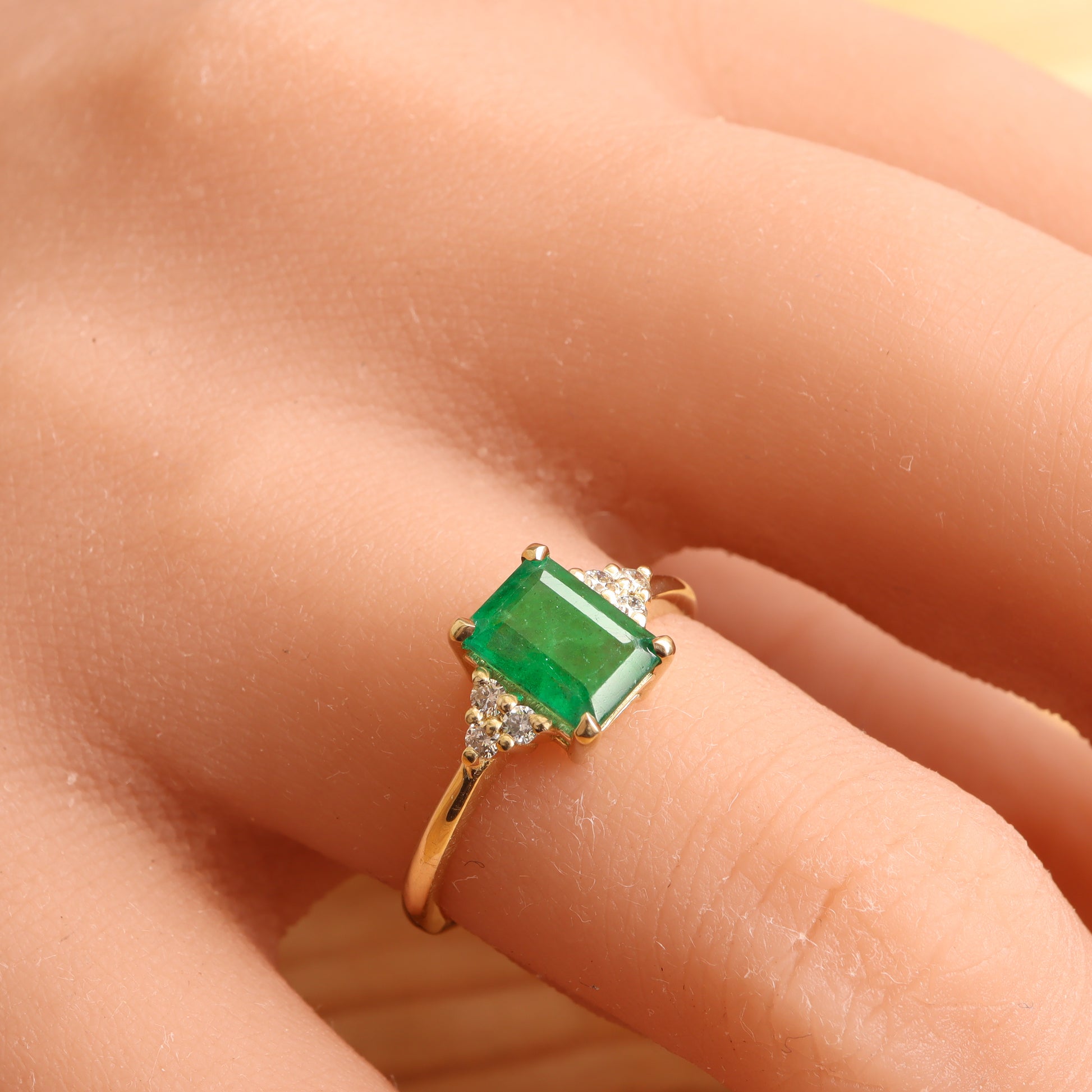 Stunning emerald engagement ring with diamonds on its sides worn on a woman's finger.