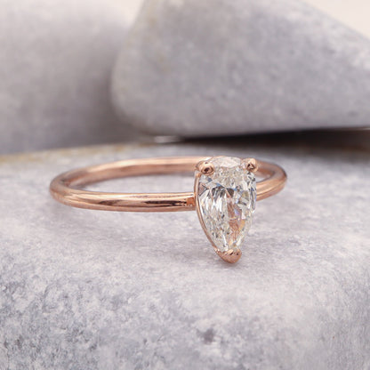 3 Prong Solitaire Pear Diamond Ring in Rose Gold on Grey Stone Background.