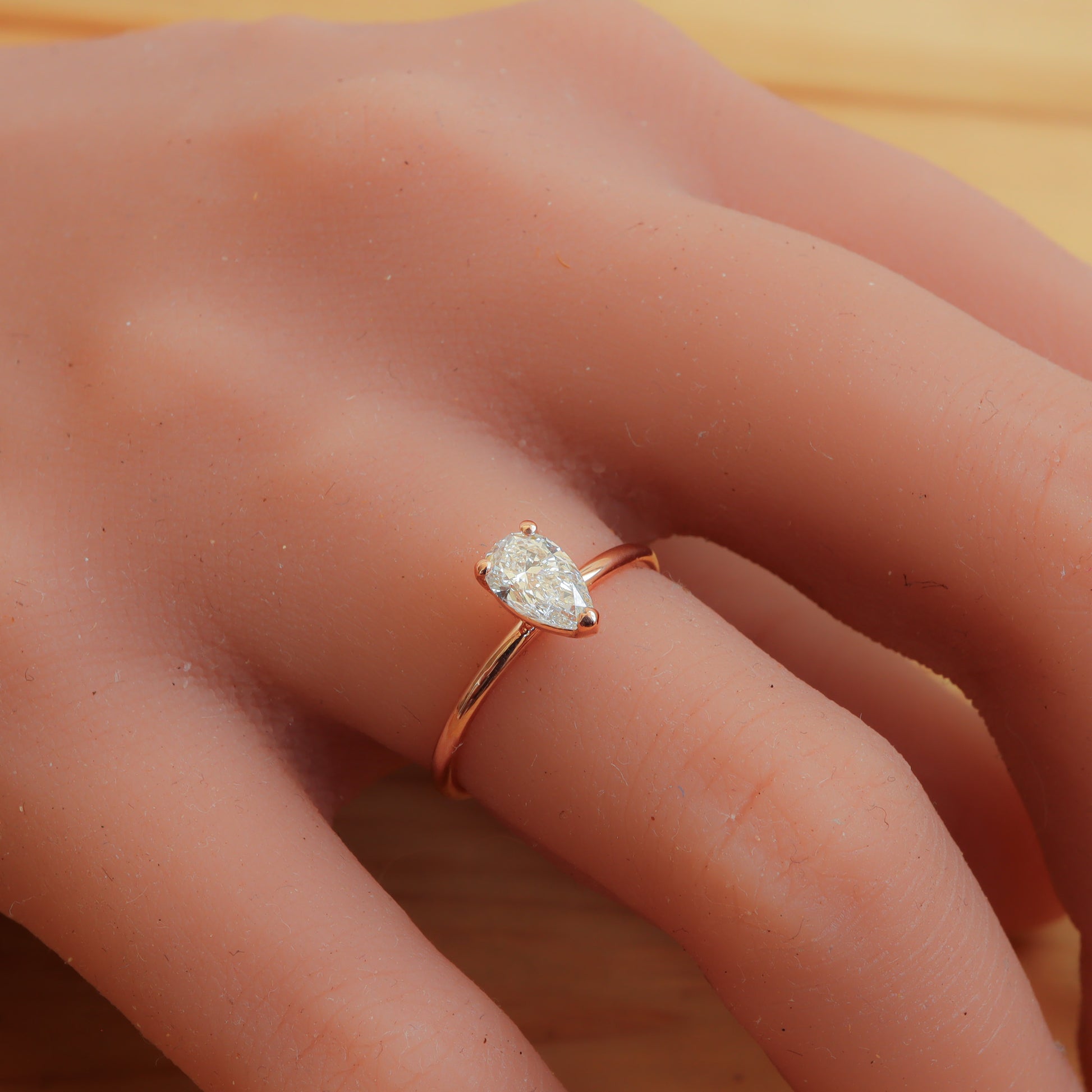 Three claws rose gold engagement ring featuring a dainty pear shape diamond.