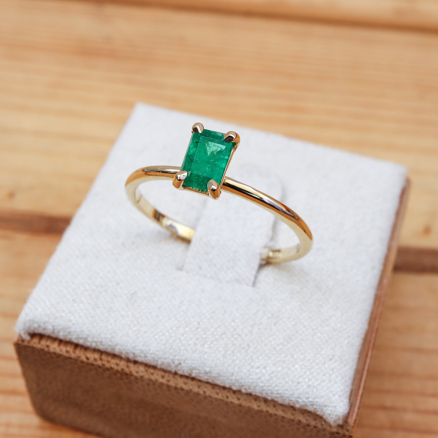 Solitaire ring featuring a baguette-shaped emerald set in gold, elegantly displayed within a wooden jewelry box.