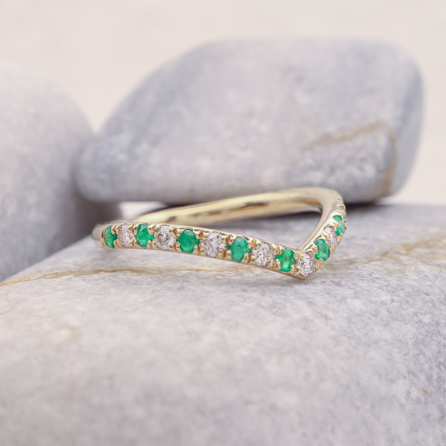 Gold Curved Emerald and Diamond Eternity Stacking Ring on grey stone, showing its profile.