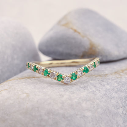 Gold Curved Emerald and Diamond Eternity Stacking Ring resting on grey stone.