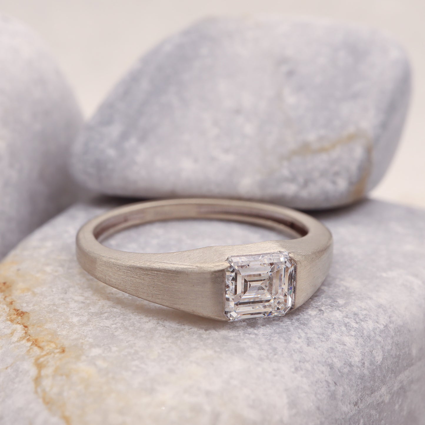 Side view of a delicate tension setting ring featuring a square emerald cut diamond in rustic white gold band.