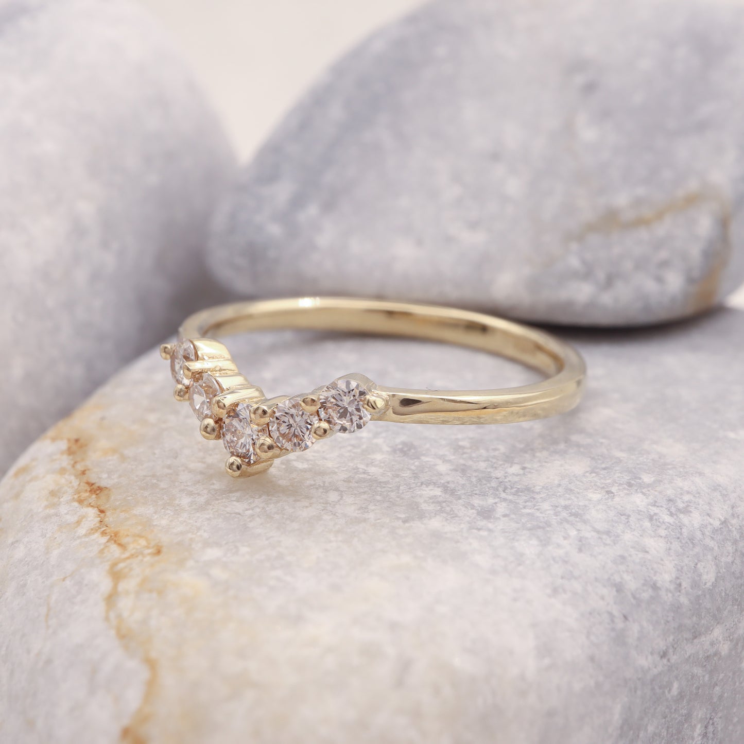 Profile view of our gold diamond curved band, displayed on a grey rock.