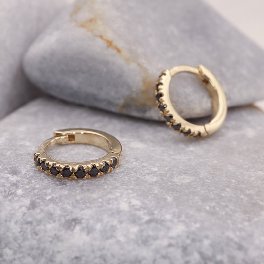 Black Diamonds Huggie Hoop Earrings in Yellow Gold displayed on a grey stone.