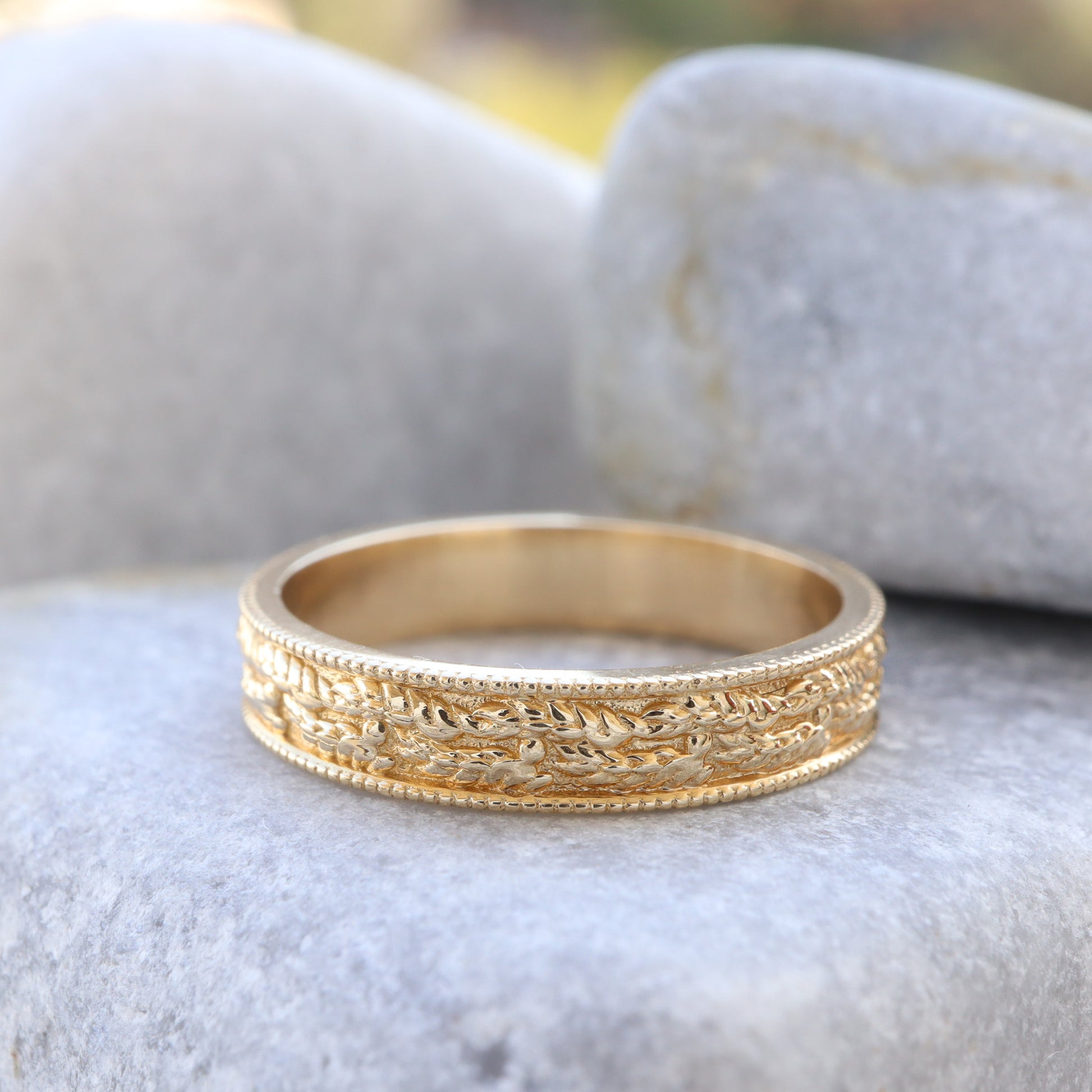 Leaf-textured and embossed gold ring displayed on a grey stone background